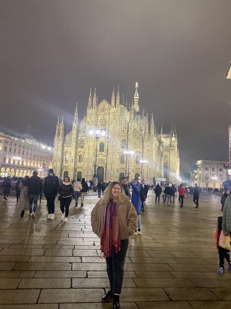 Woman stood in front of the lit up Milan Duomo in the evening 